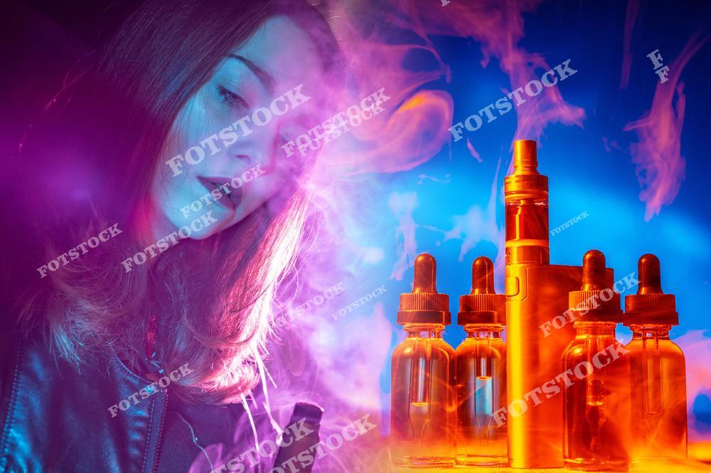 Стильное изображение девушки с электронной сигаретой и набором для вейпинга в окружении клубов пара и дыма. На фотографии представлены современные устройства для парения, жидкости и масла для вейпа, расположенные на столе рядом с аксессуарами для электронного курения. Атмосфера модного lifestyle и современной vape-культуры делает изображение идеальным для рекламы интернет-магазинов электронных сигарет, vape shop, жидкостей для вейпа и аксессуаров для парения. Фотография отлично подойдет для маркетинговых материалов, баннеров, блогов о вейпинге и публикаций, связанных с продажей электронных сигарет и товаров для вейперов.